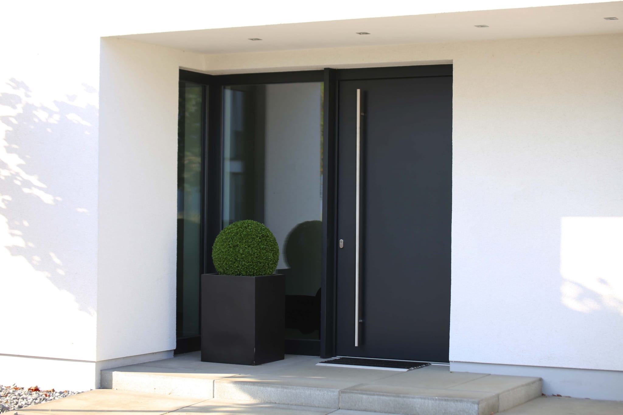 Eine moderne Eingangstür in eleganter Anthrazit-Farbe mit einer langen vertikalen Griffstange aus Edelstahl.