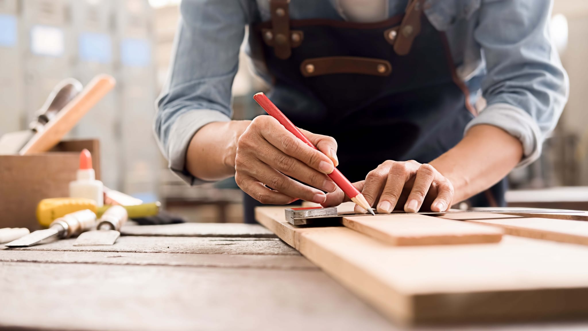 Ein Heimwerker macht eine Markierung auf einem Stück Holz mit einem Zimmermannsbleistift in einer Werkstatt