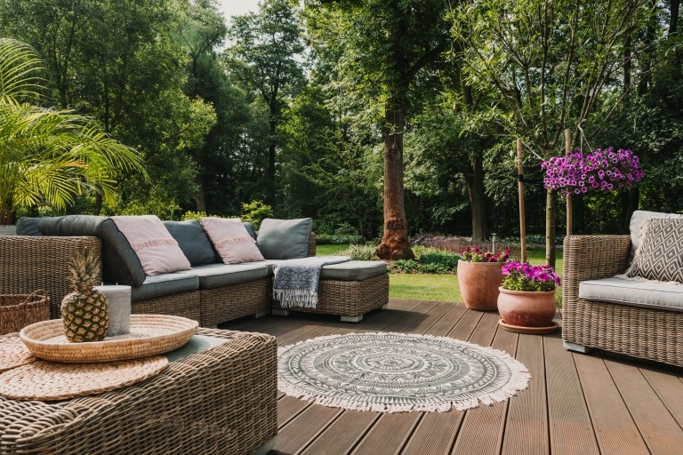 Gartenmöbel auf einer schönen Holzterrasse vor einer schönen Gartenanlagenkulisse mit Bäumen und Pflanzen.