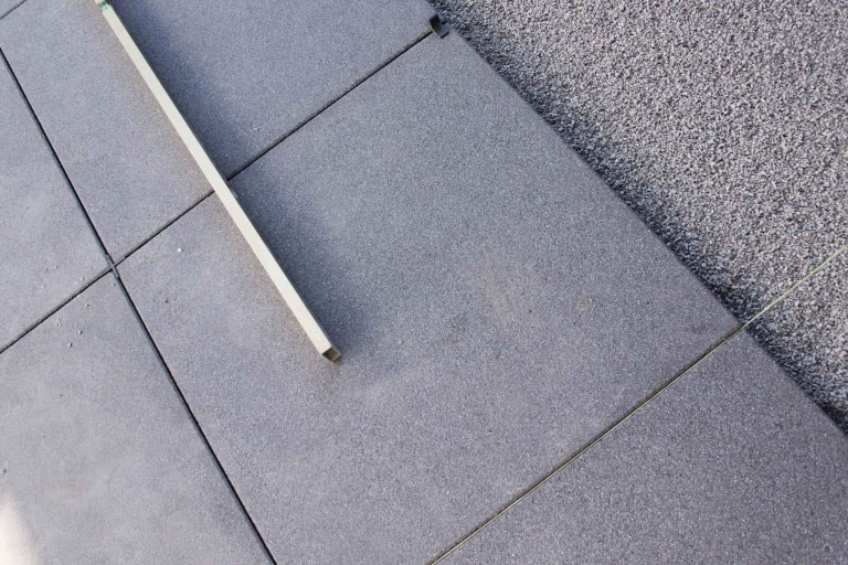 Großflächige graue Betonsteinplatten werden auf ein feines Kies oder Sandbett mit HIlfe von Lehren und Schnüren verlegt.