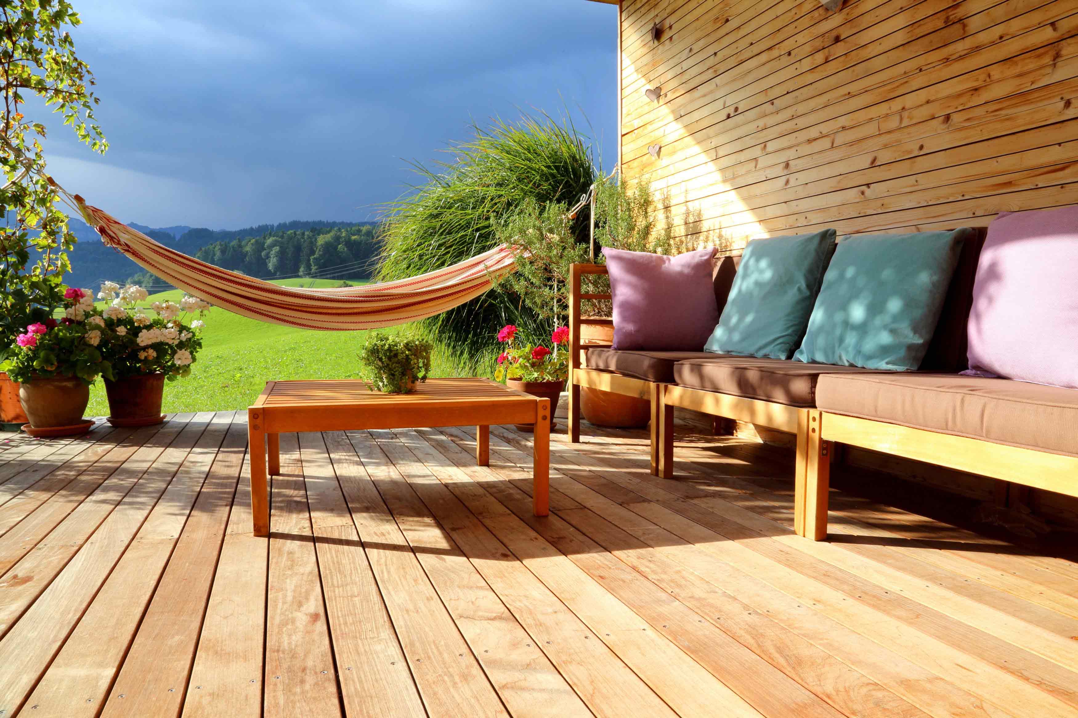 Eine Terrasse aus hellen Holzdielen mit Holzmöbeln einer gemütlichen Hängematte mit einer schönen Hügellandschaft im Hintergrund.